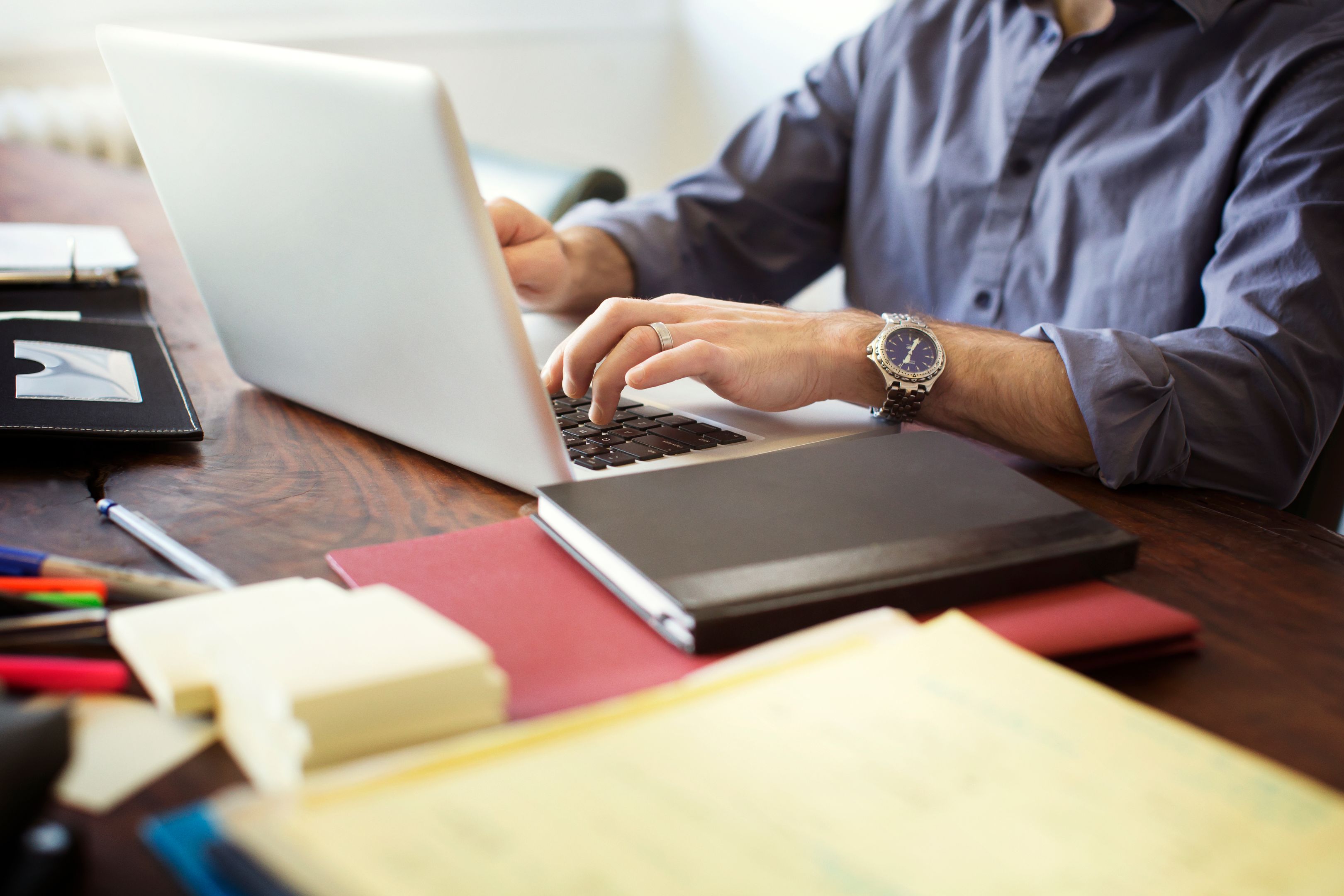 A person working on their laptop with lots of files around them on the table.