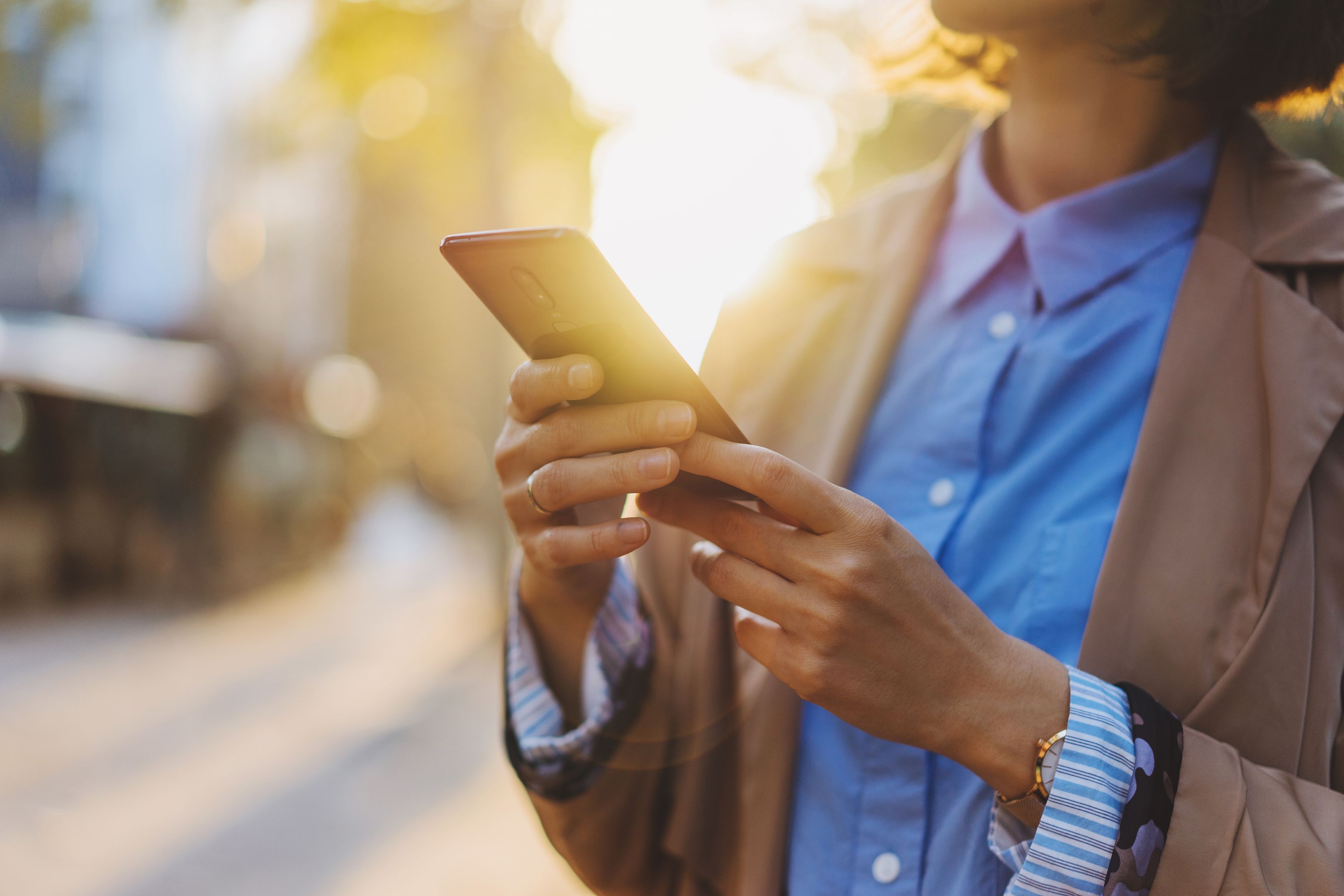 A person holding their mobile device in a city in the morning.