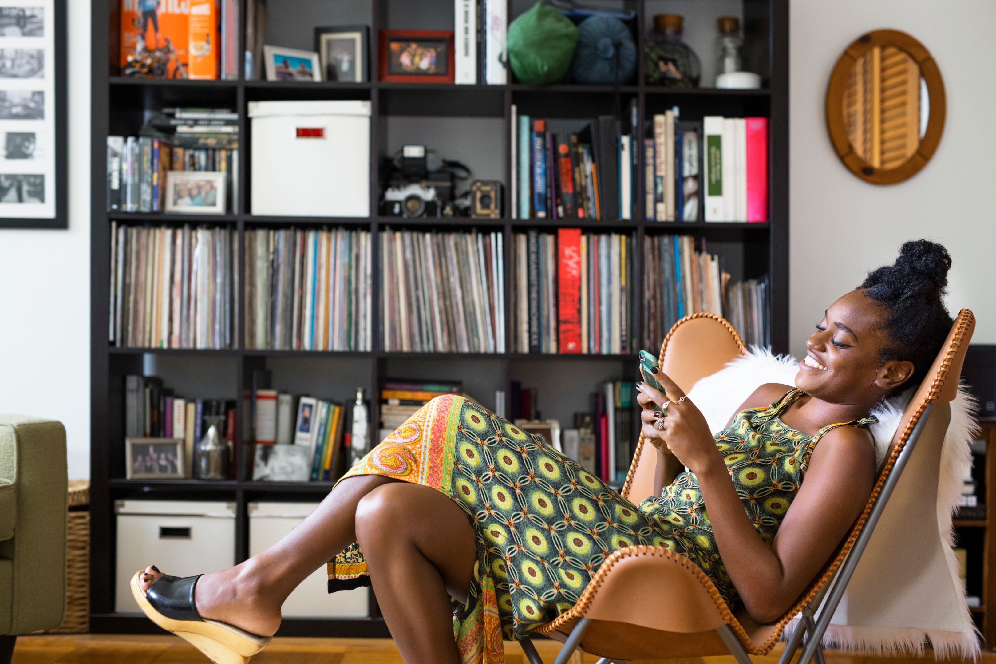 A person relaxes in a chair at home and smiles while reading on their phone.