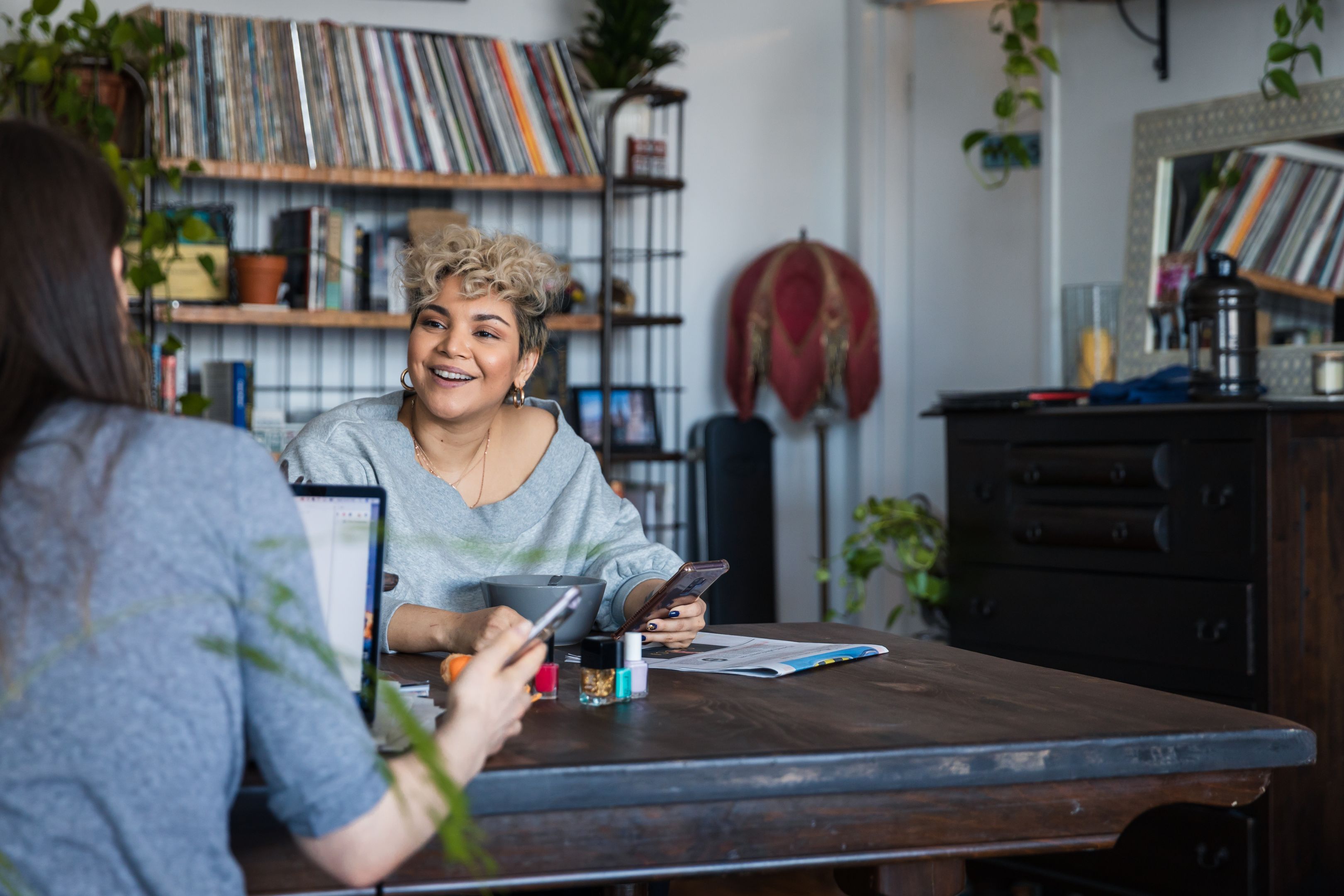 Two people work on their mobile devices at a table in a living room.