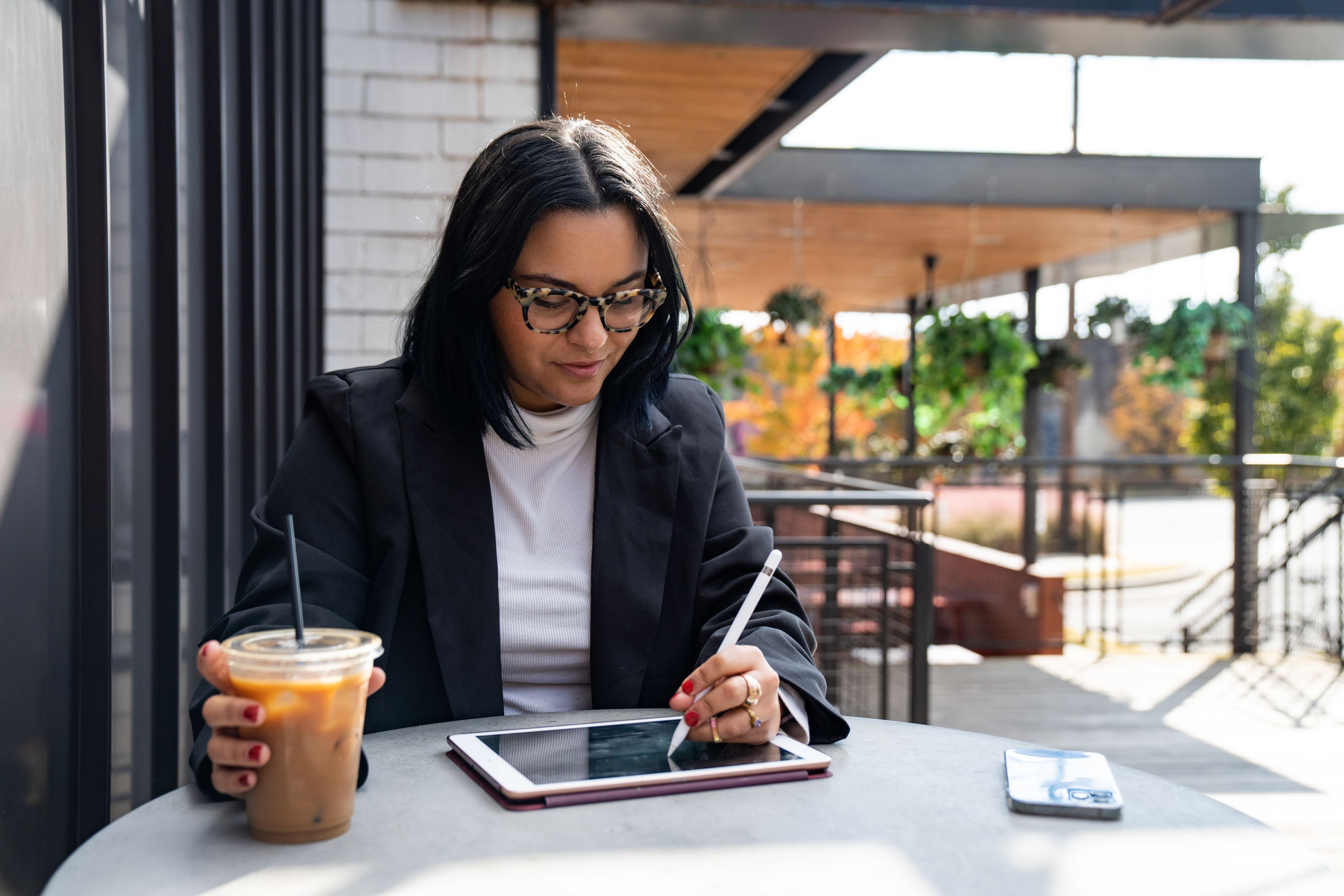 A person works with a tablet and pen with an iced coffee.