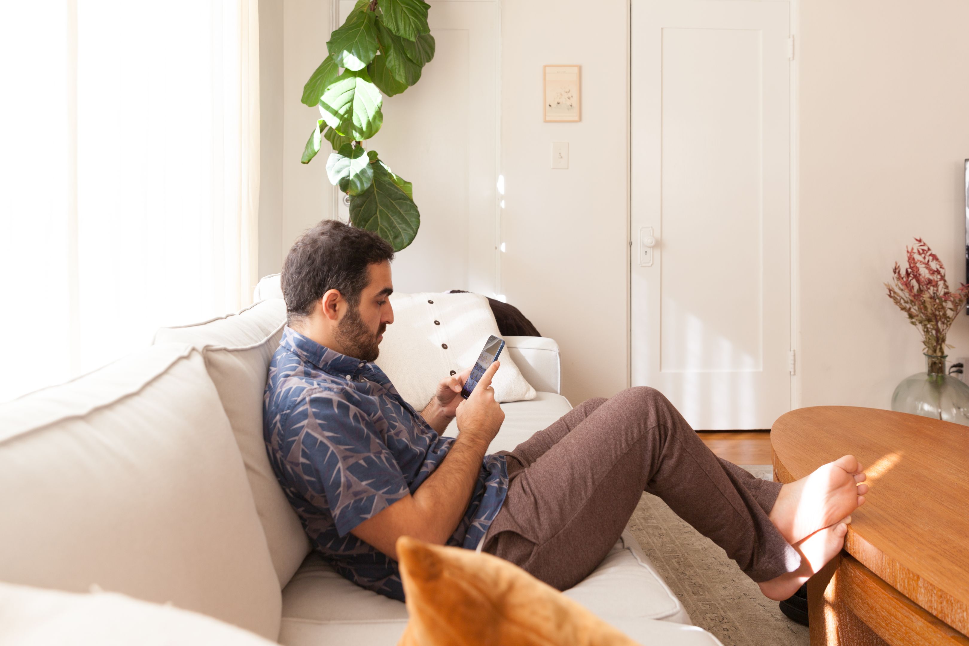 A person sat on a sofa on their mobile device with their feet resting on the coffee table in front of them.