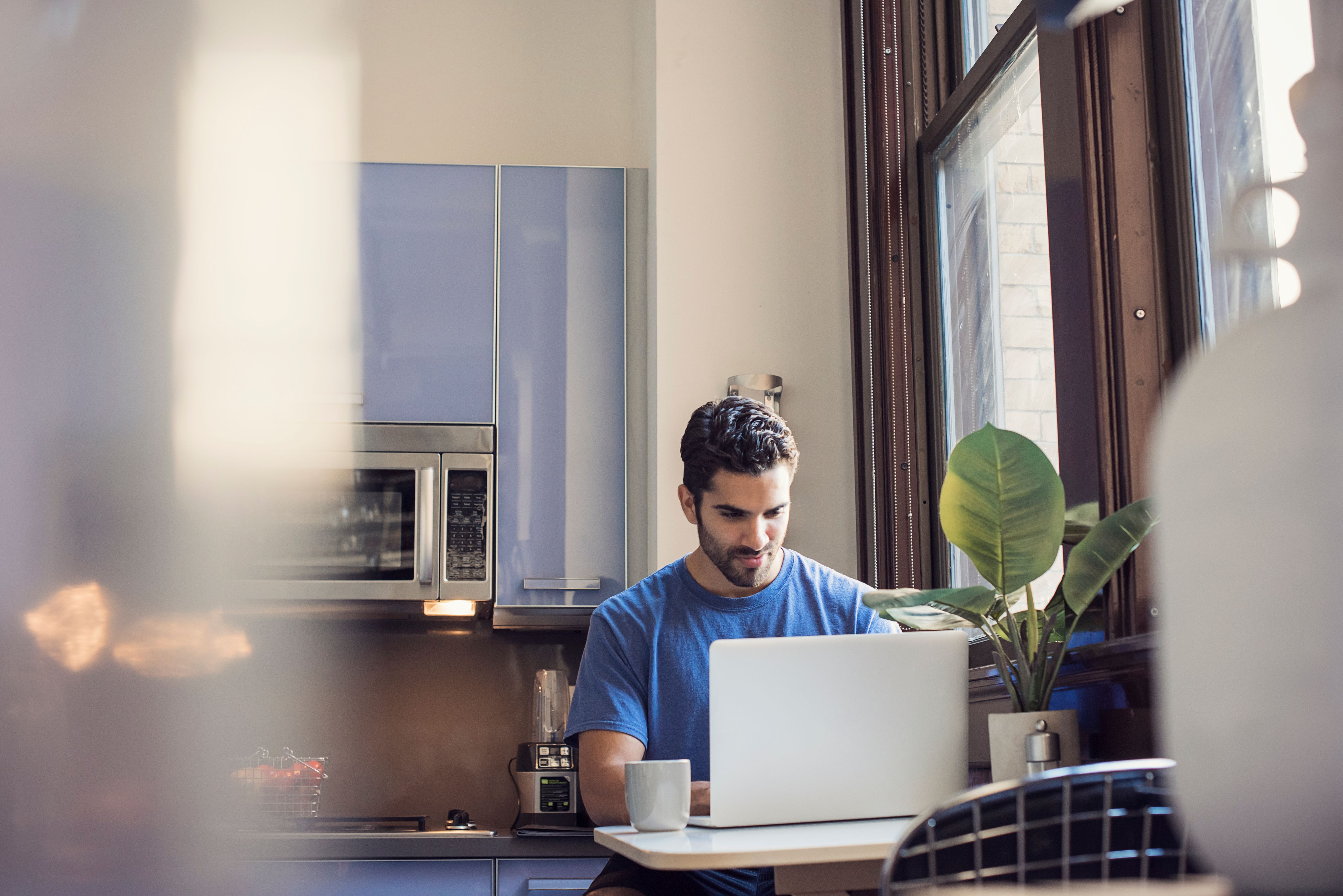 A person works on a laptop while sitting in the kitchen.