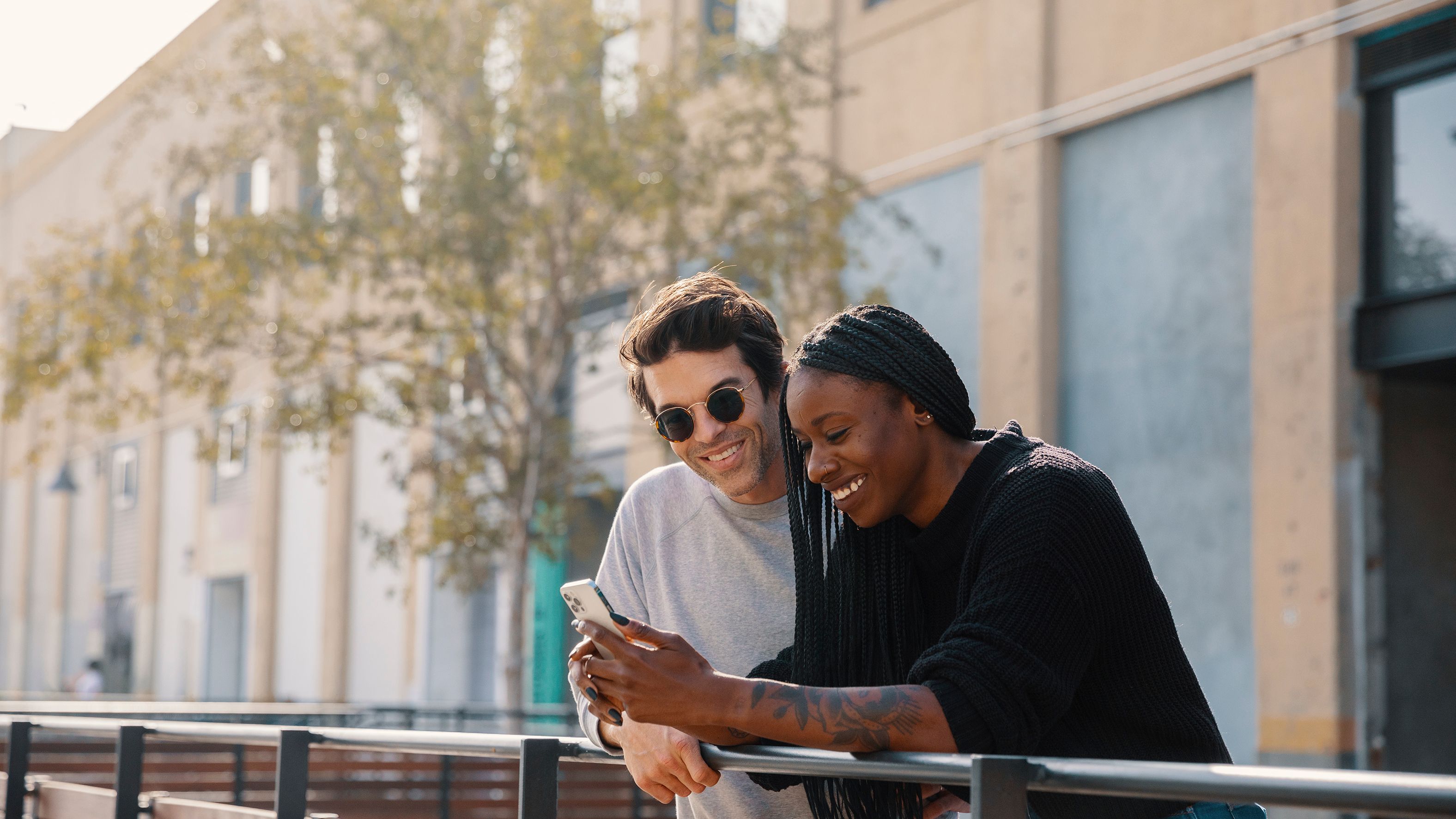 Two people in a city smile looking at a mobile device.