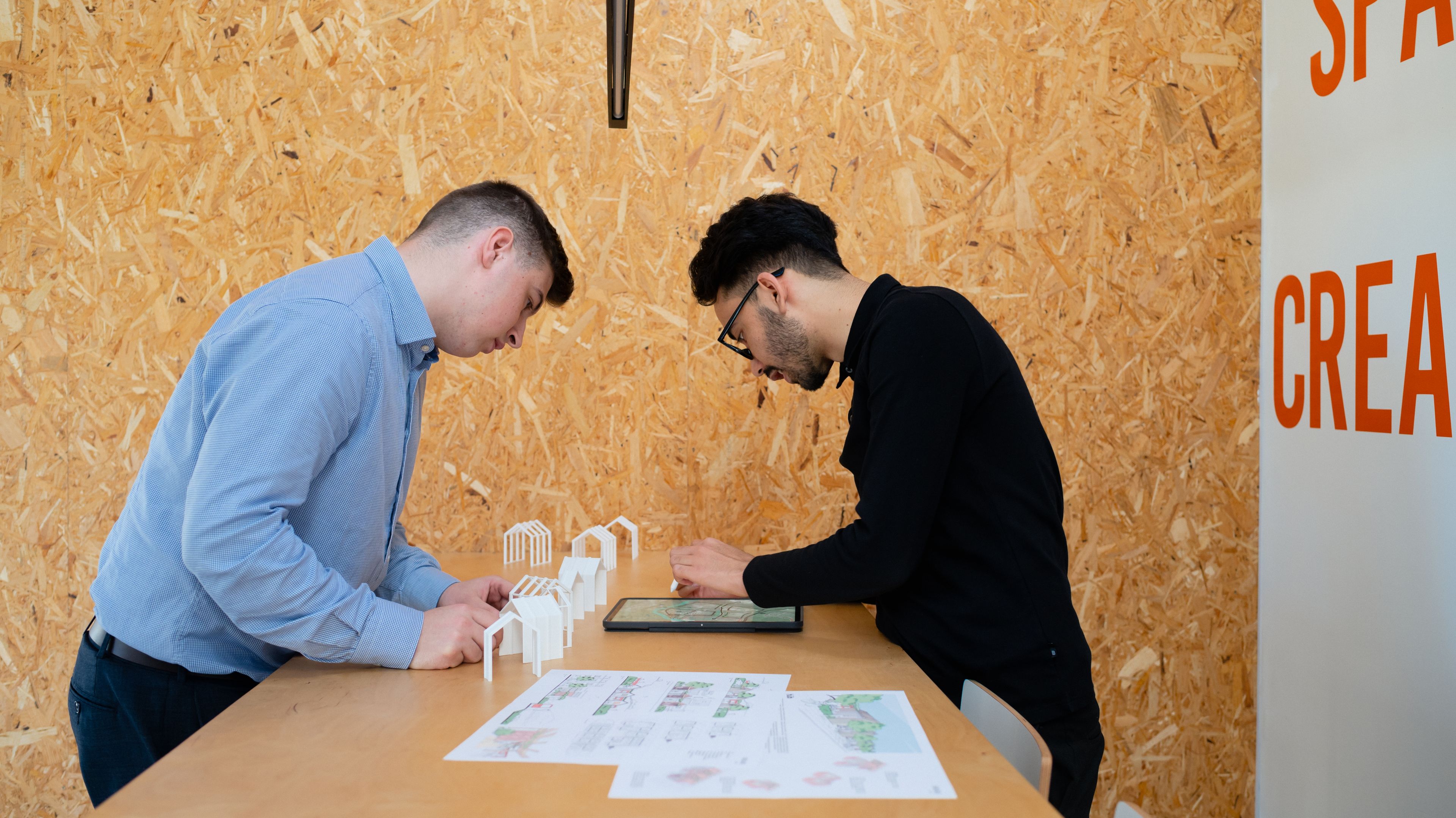 Two people work together at a standing desk with a tablet and paperwork.