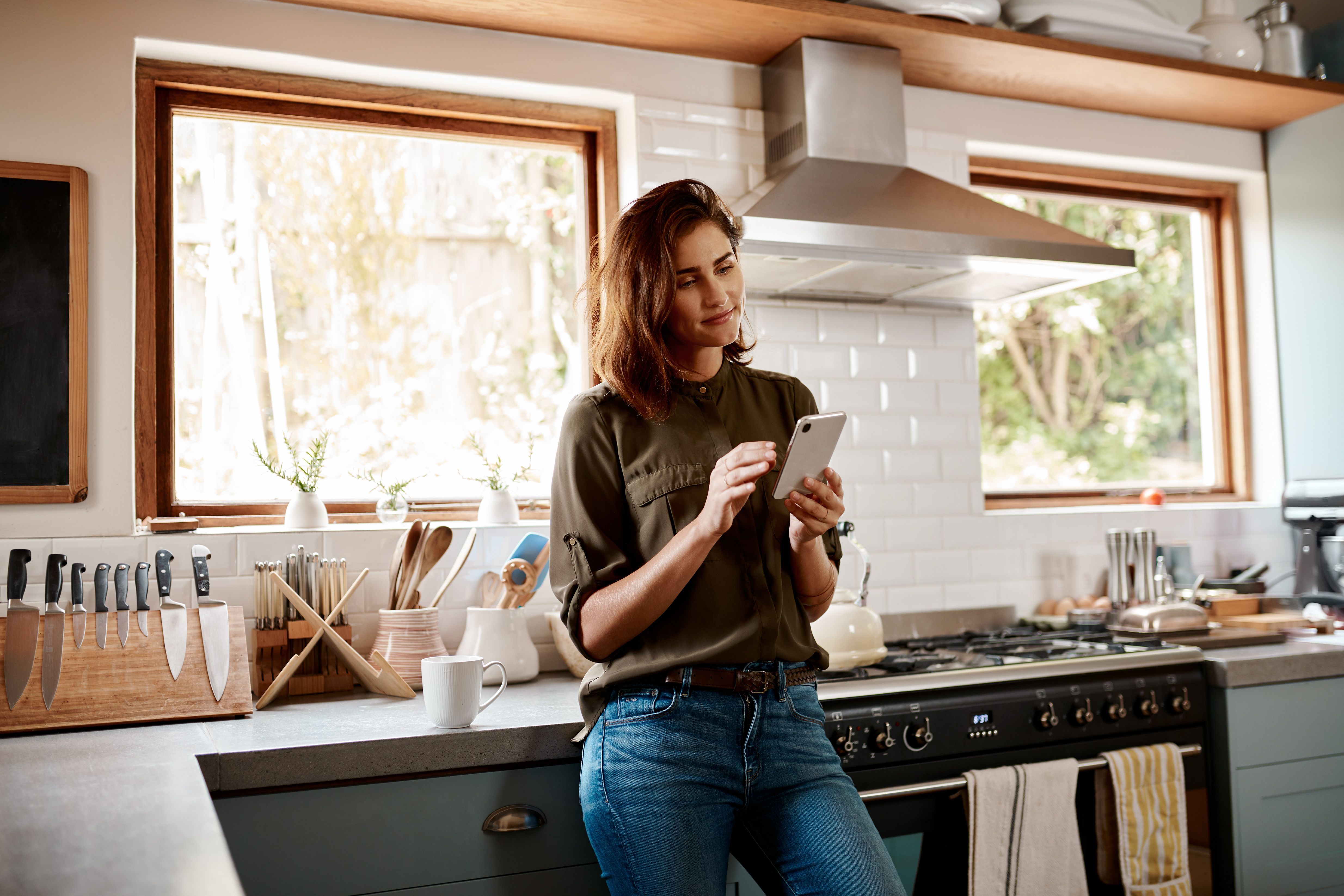 A person stands in their kitchen looking at their mobile device.