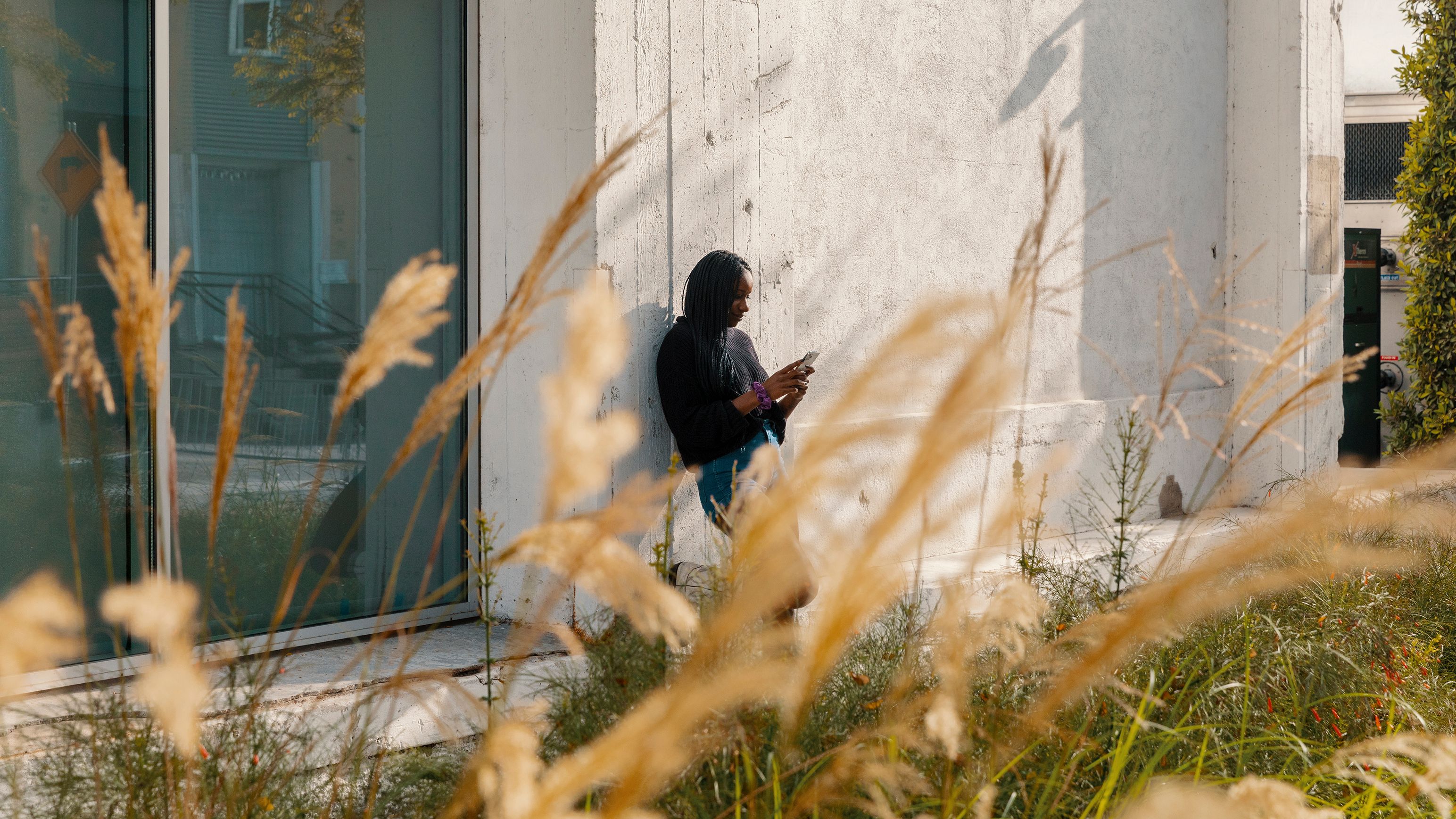 A person leaning against a building outside while on their mobile device.