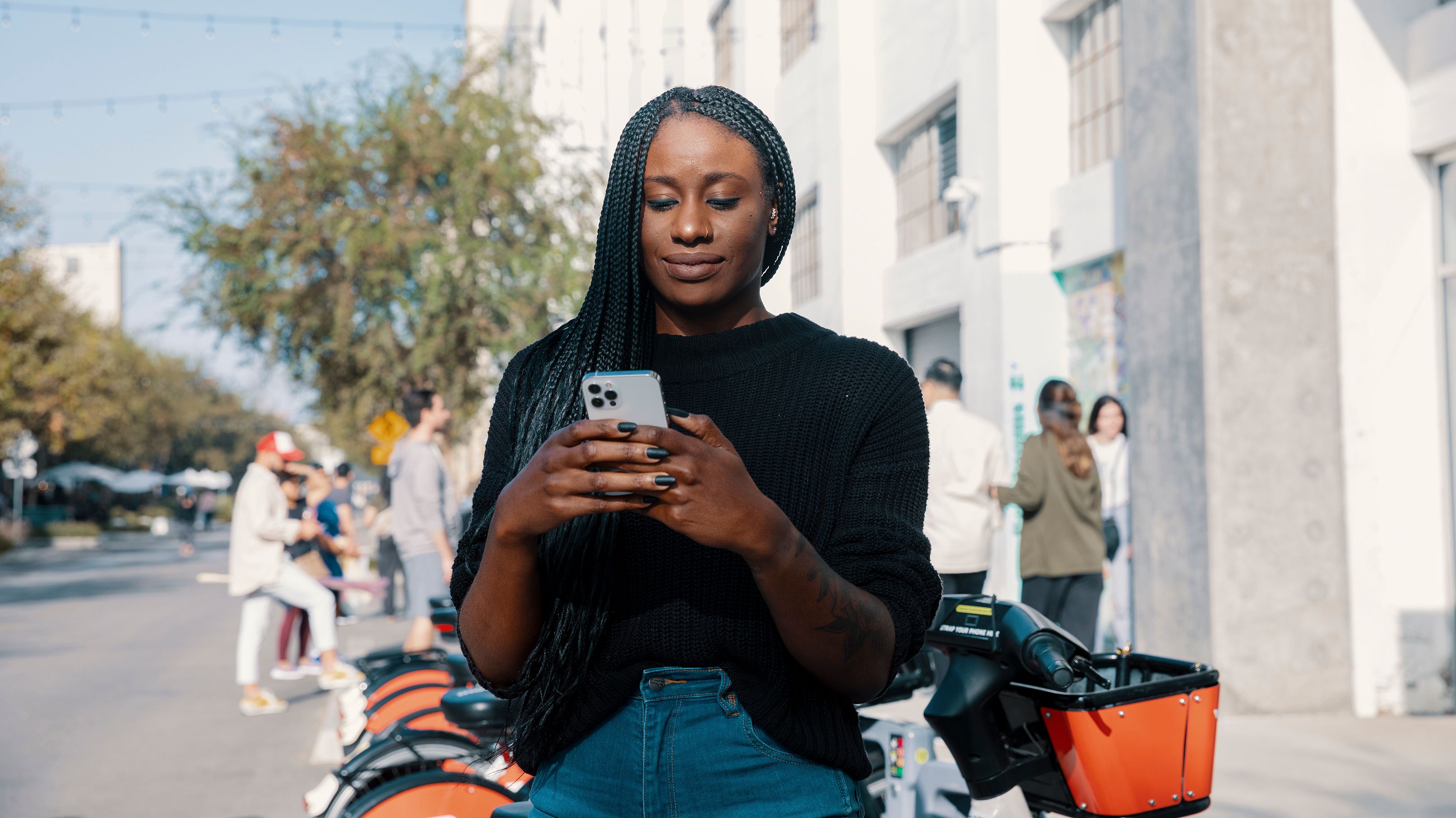 A person stands on a road in front of bicycles while looking at their mobile device.