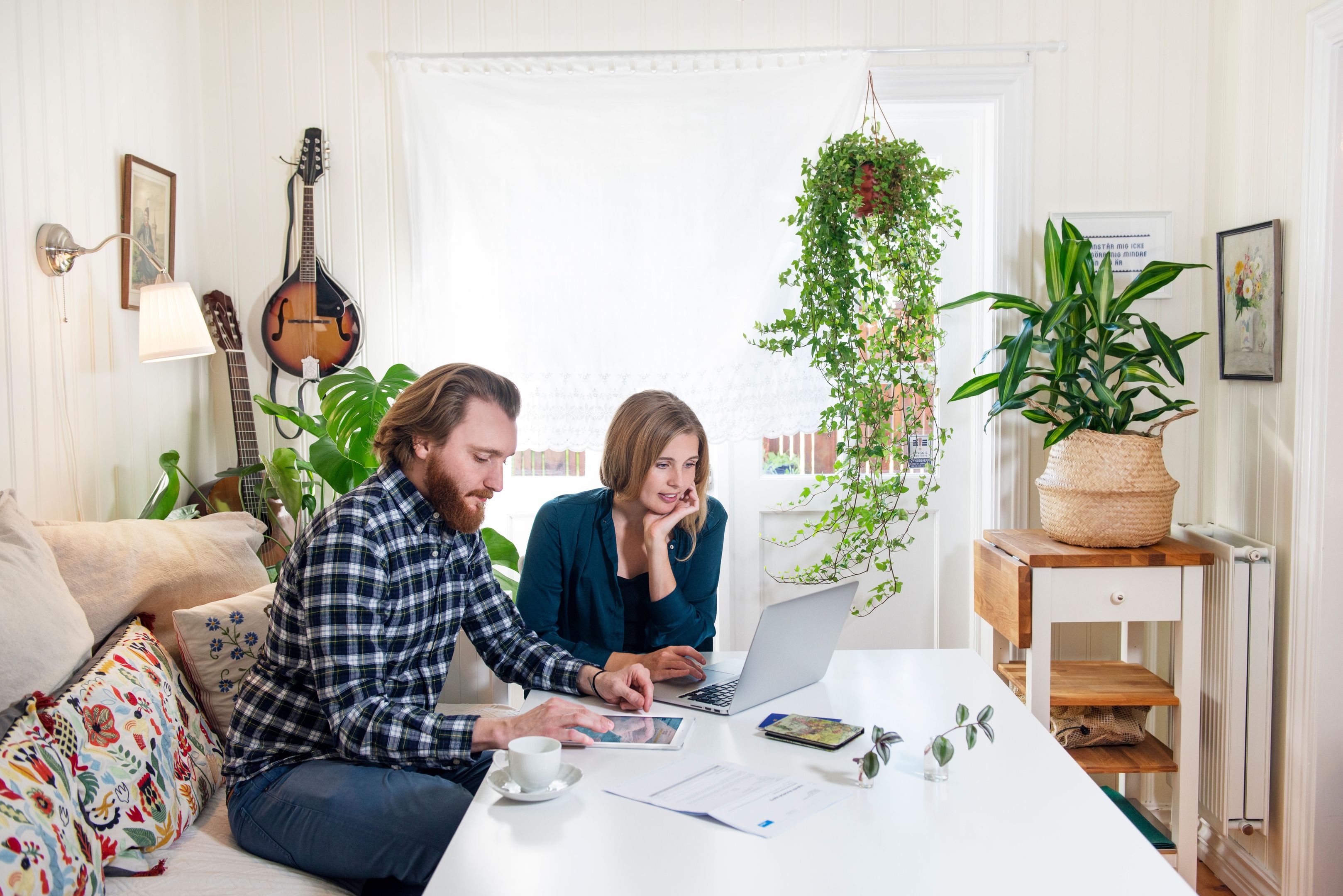 Two people work from a tablet and a laptop on a coffee table in their home.