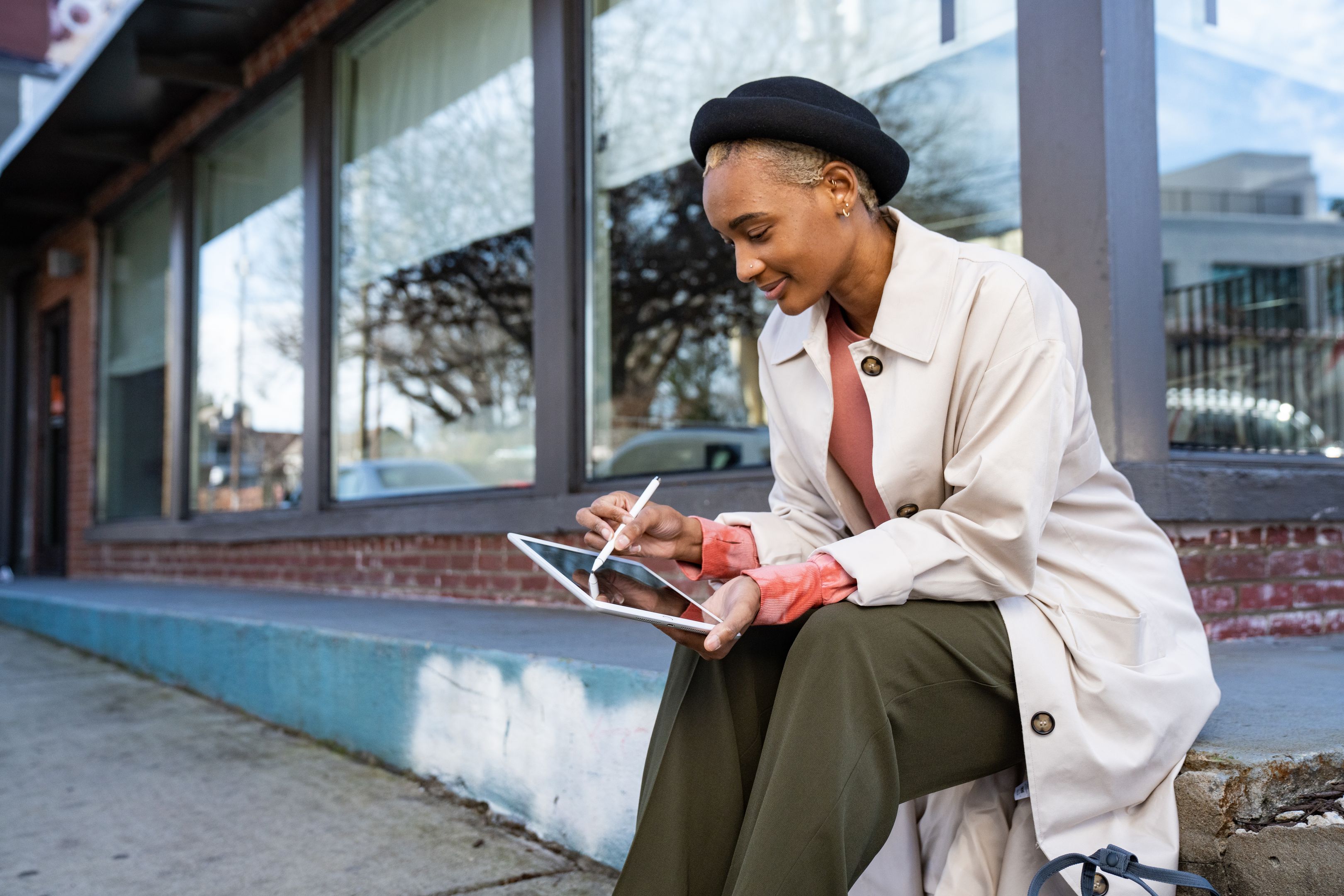A person sits on a street corner using a tablet with a pen.