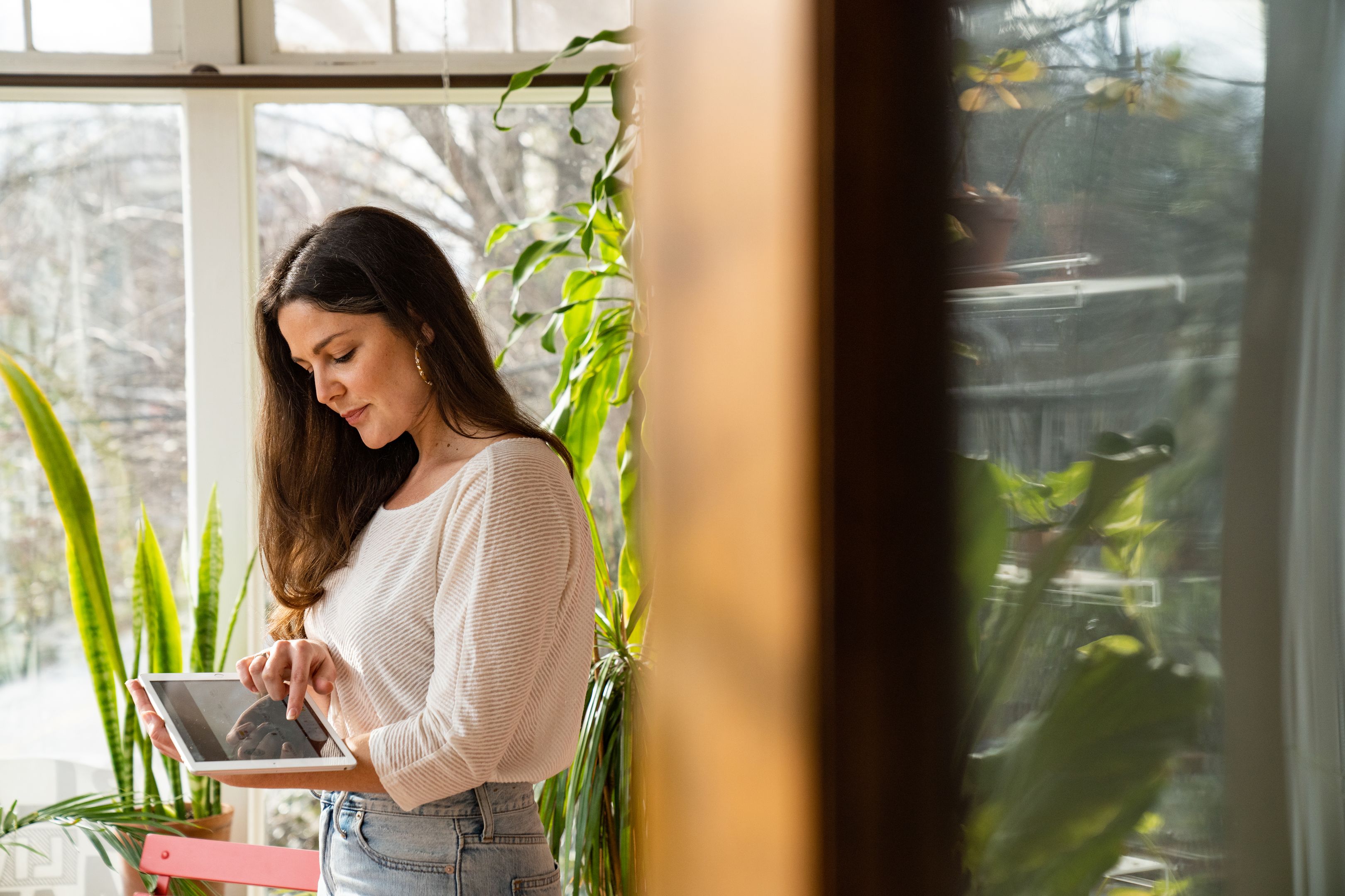 A person looks at a tablet while standing in a naturally-lit room.