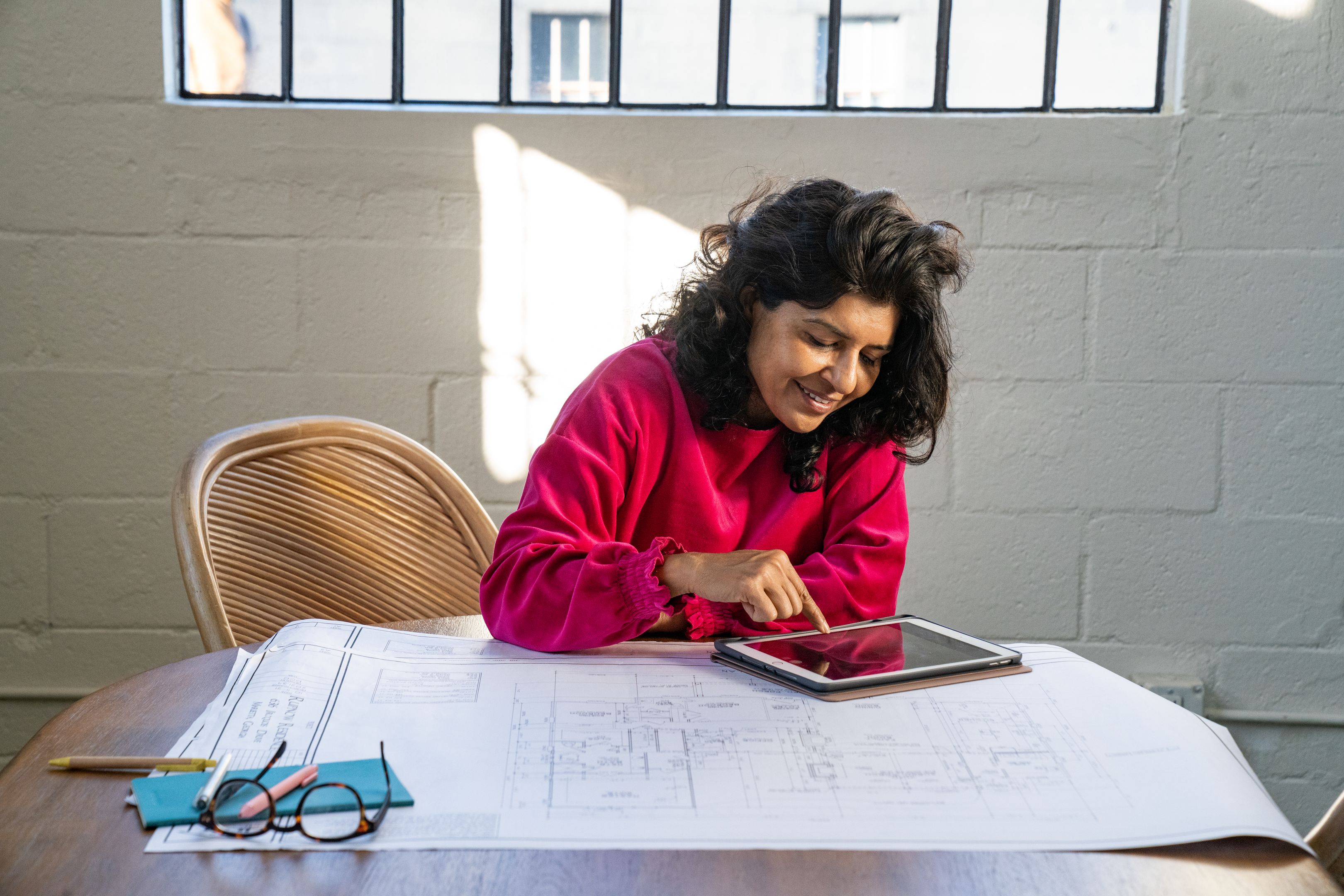 A person works with a tablet and some blueprints.