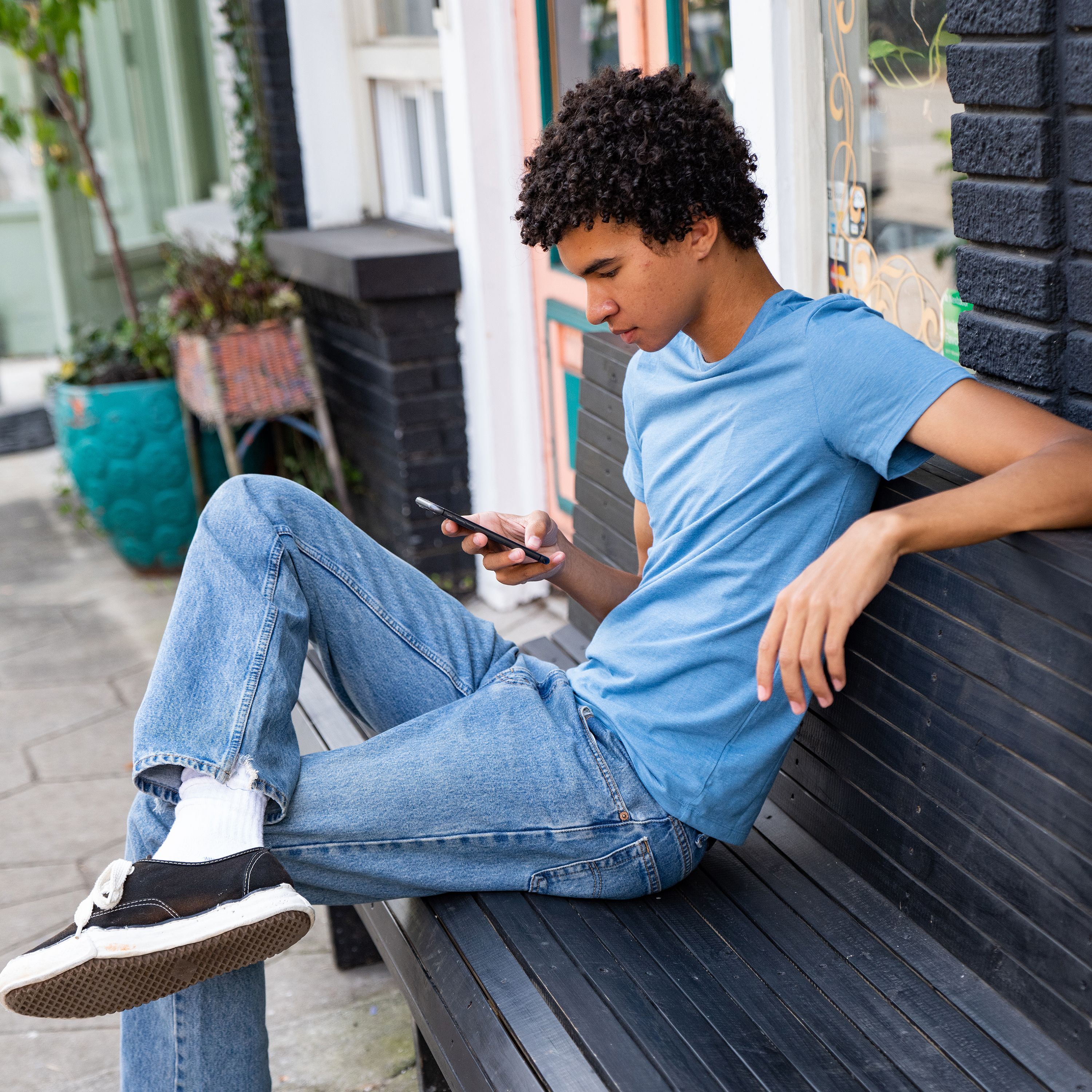 A person relaxes on a bench while looking at their mobile device.