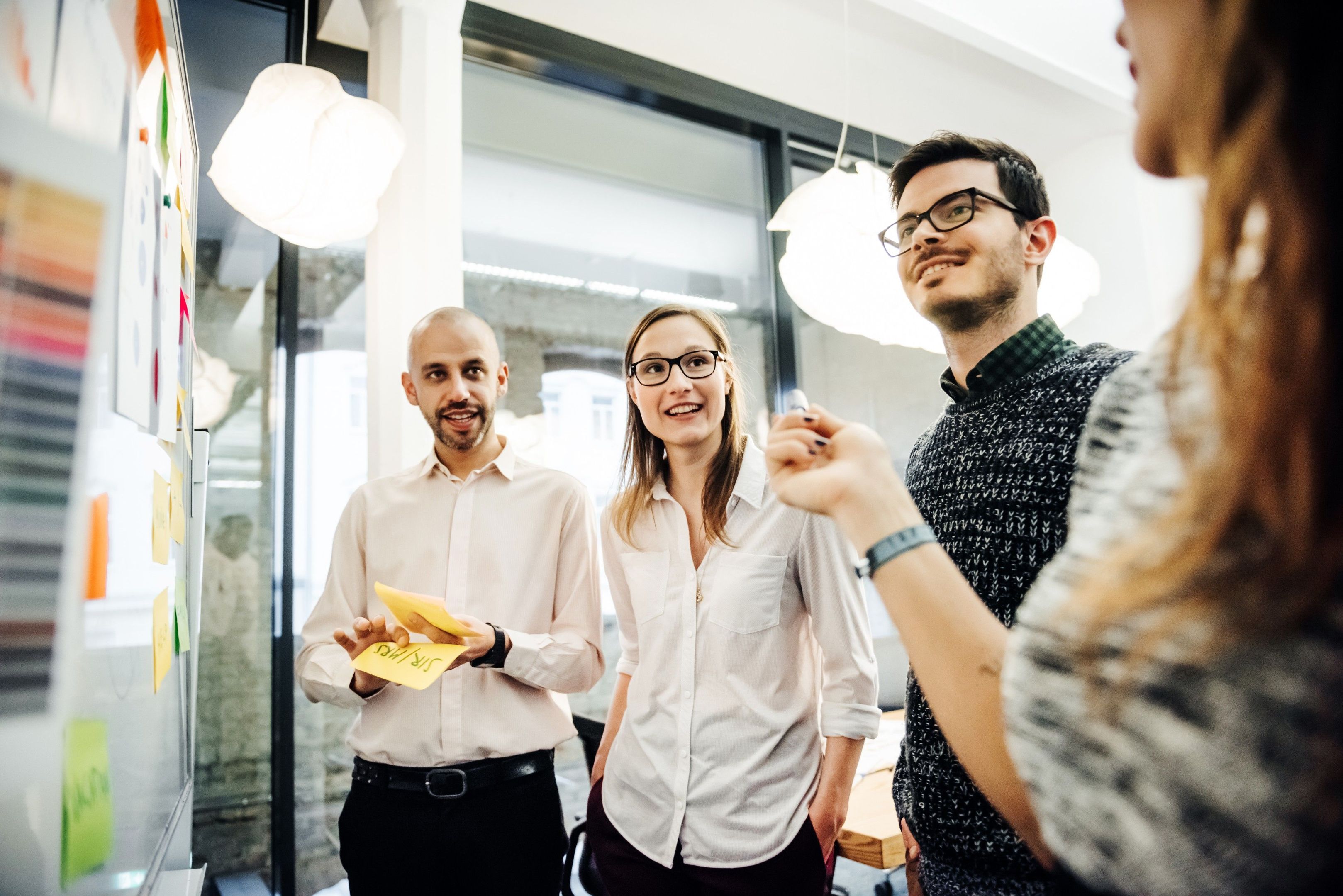 Group of people standing and discussing ideas with sticky notes on a whiteboard.