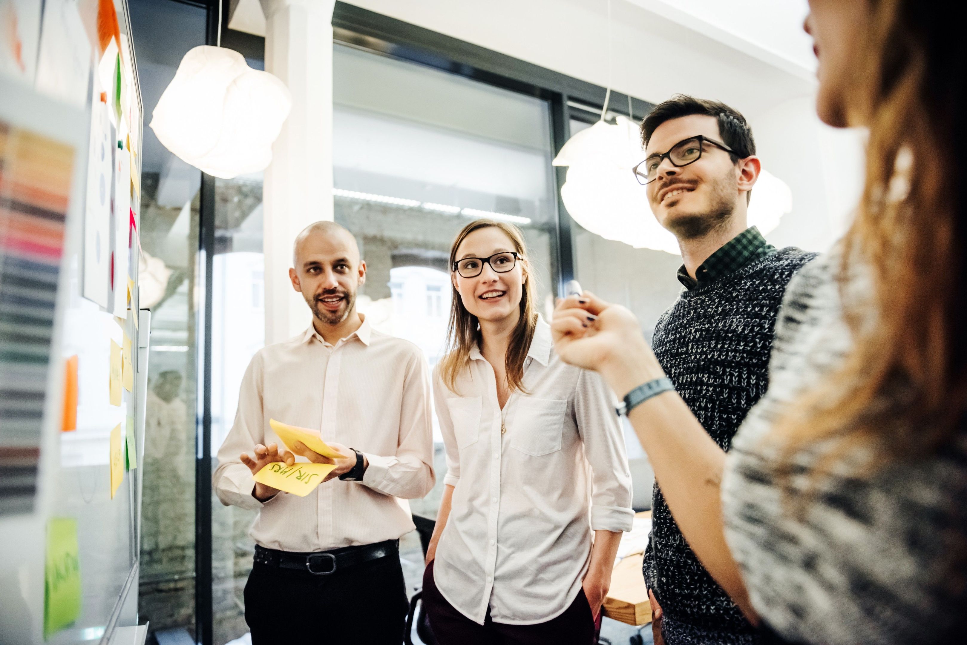 Four people stand in front of a whiteboard collaborating on ideas.