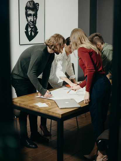 A group of four people gathered around a table in a modern office space, collaborating on a project