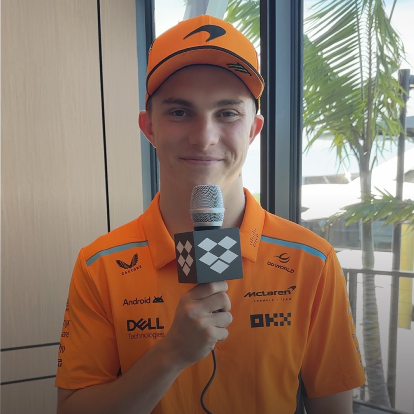 Lando Norris devant une voiture de course McLaren et tenant une boîte avec le logo Dropbox