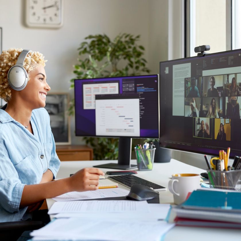 A person wearing headphones smiles during a virtual teambuilding call, with multiple colleagues visible on one monitor.