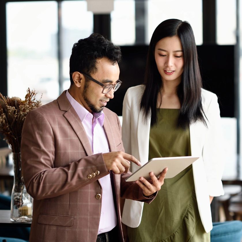 Two people standing in an office look at a tablet device one of them is holding and discuss using eSignatures in their business.