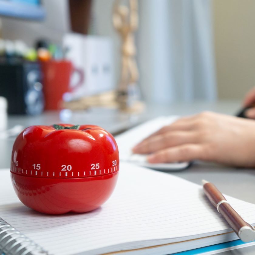 A person working on a task has a Pomodoro timer set on their desk.