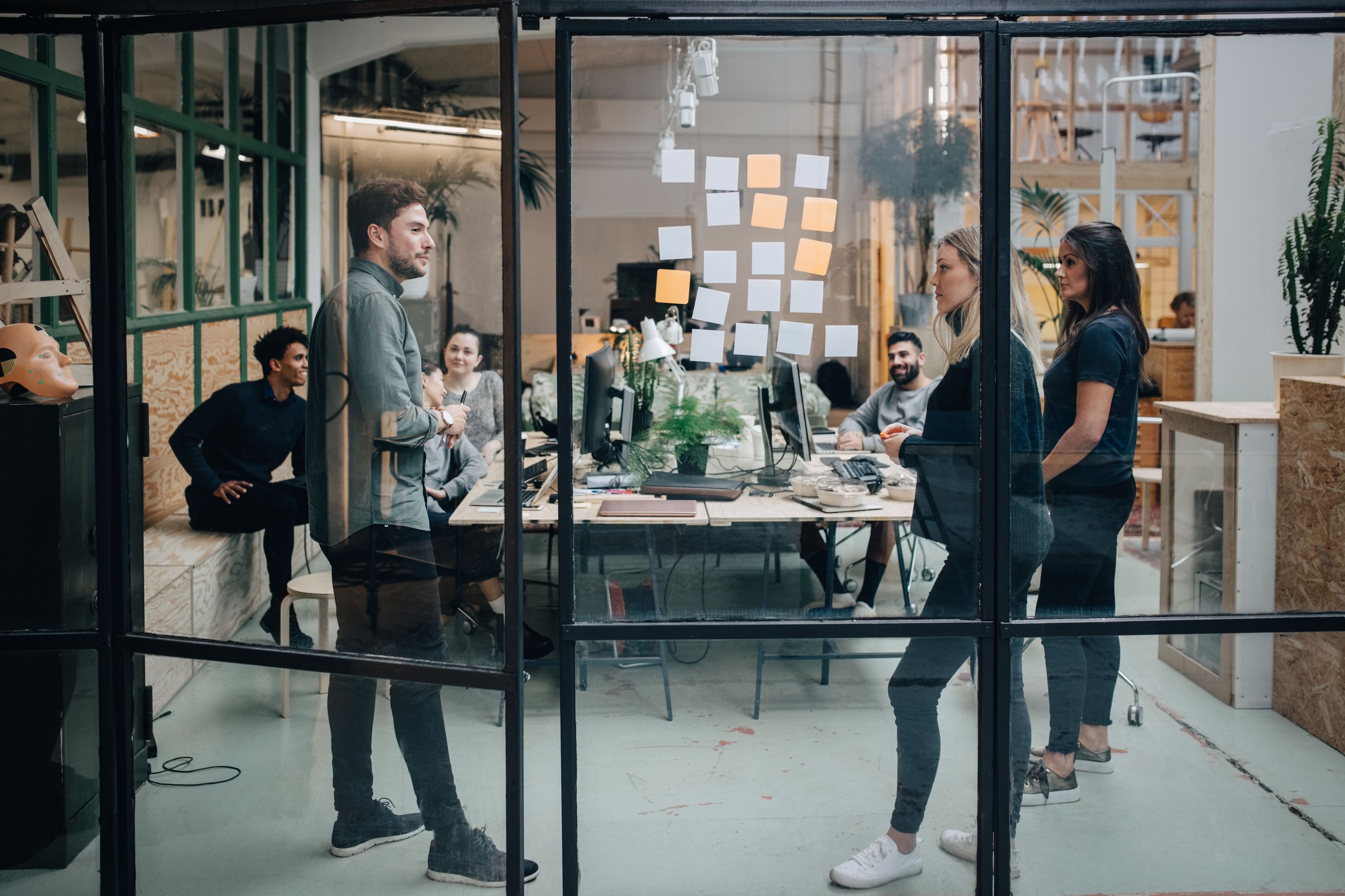 Marketing team gathers in an office space with sticky notes on glass, planning workflows and brainstorming ideas together.