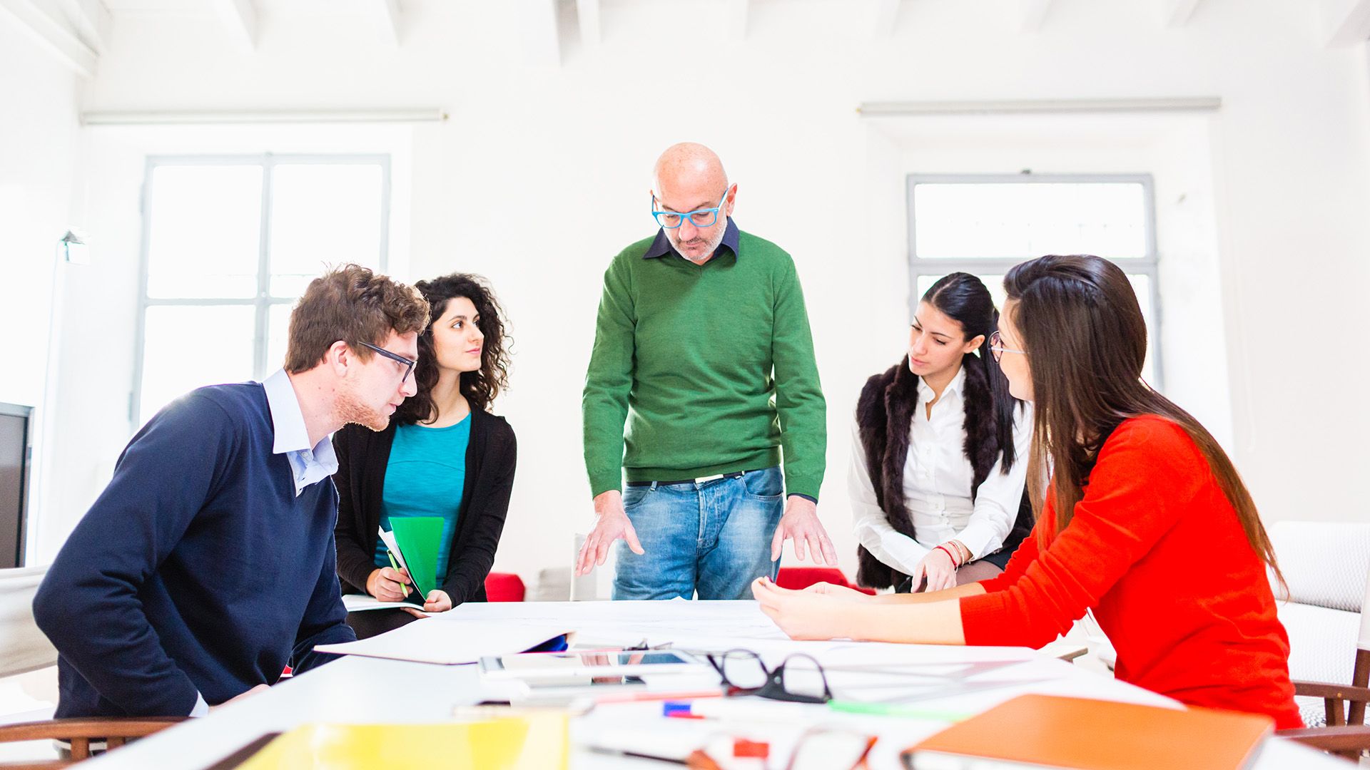 A team of engineers map out their construction project on a boardroom desk covered in plans.