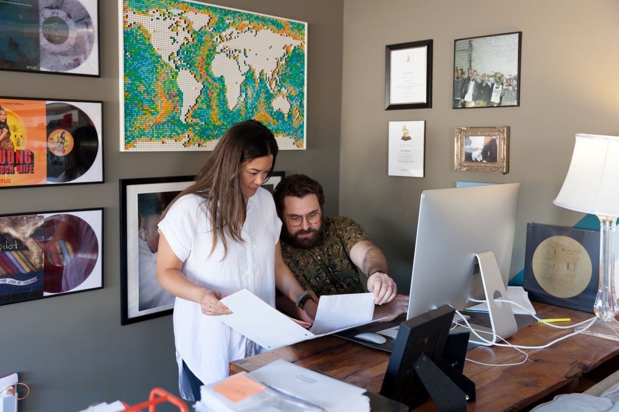 Two people look at some documents together while working at a desk.