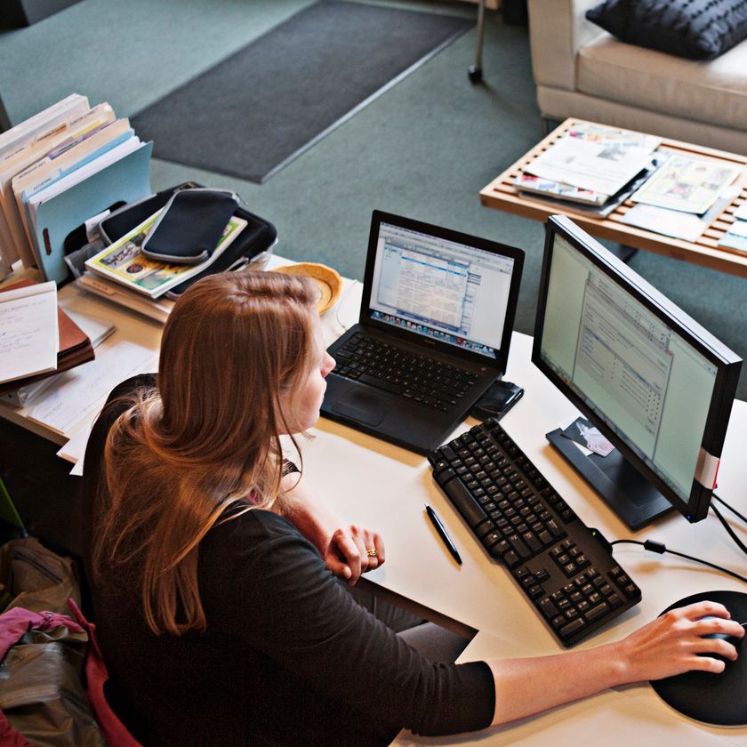 A woman working on her computer with two screens for a cluttered desk