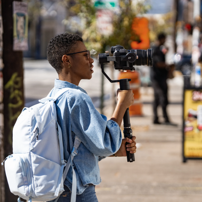 A videographer holds a professional camera mounted on a stabilizer as they capture raw footage to send to a video editor.