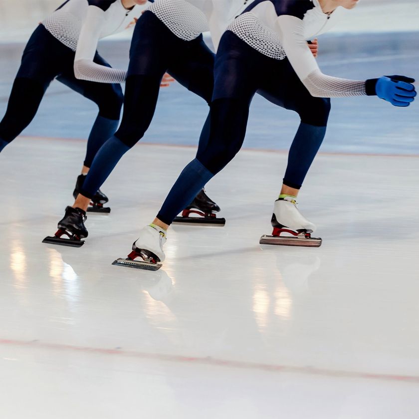 Pro speed skaters race on an indoor ice rink wearing aerodynamic suits and specialized ice skates in a speed skating event.