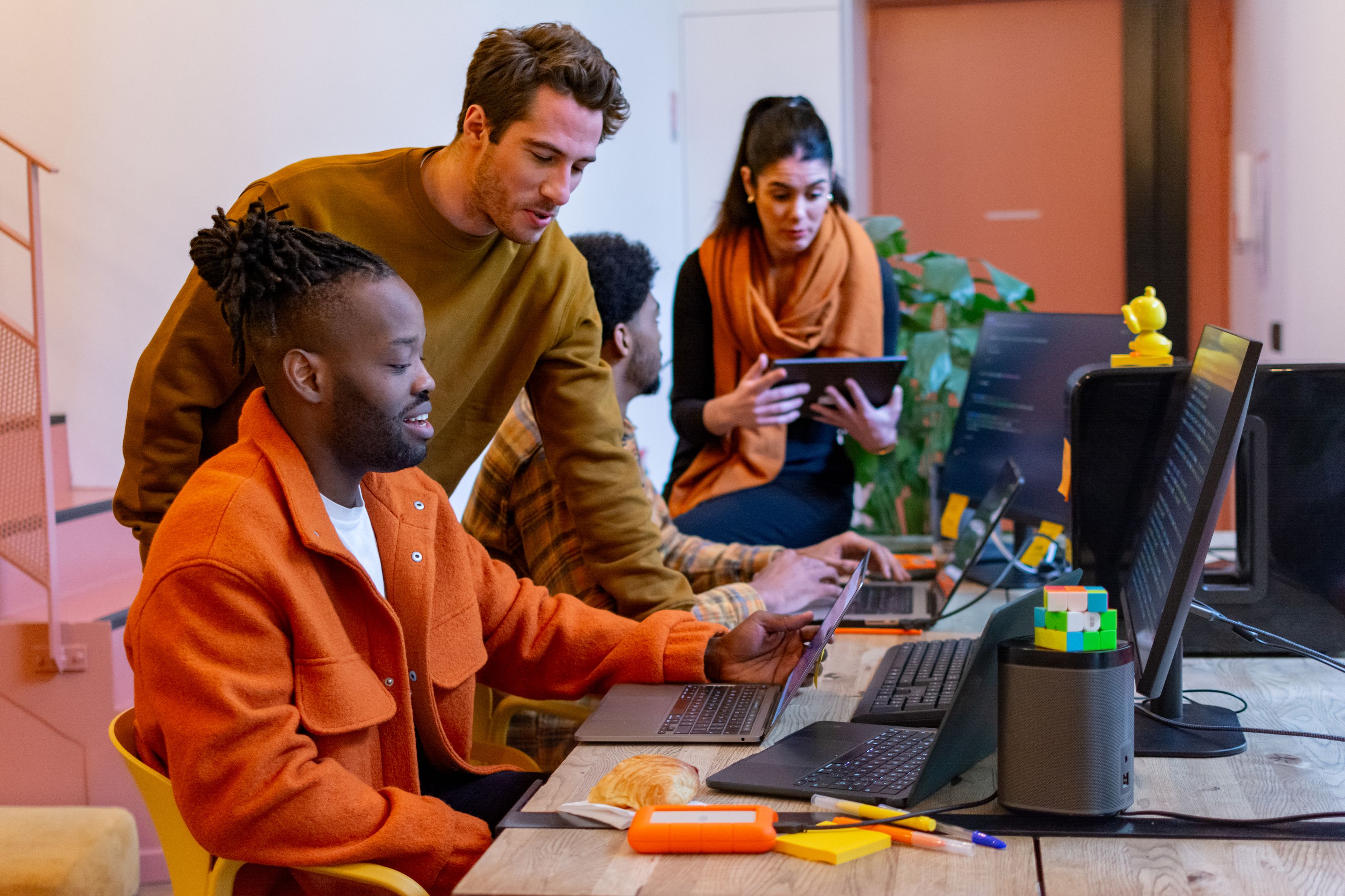 Une équipe travaille sur des ordinateurs portables tandis qu’un collaborateur utilise une tablette, illustrant la collaboration et l’édition en temps réel dans un environnement professionnel.