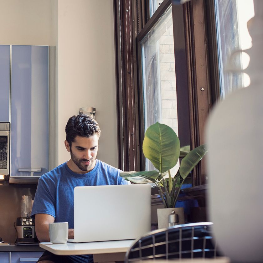 Person sitting at a table working on a laptop in a bright kitchen space with a cup of coffee nearby