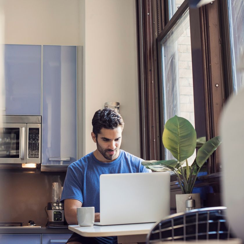 Person working on a laptop at a table in an office space kitchen.