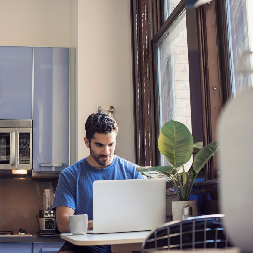 A person sitting at a table using a laptop in a modern kitchen, focused on a task.