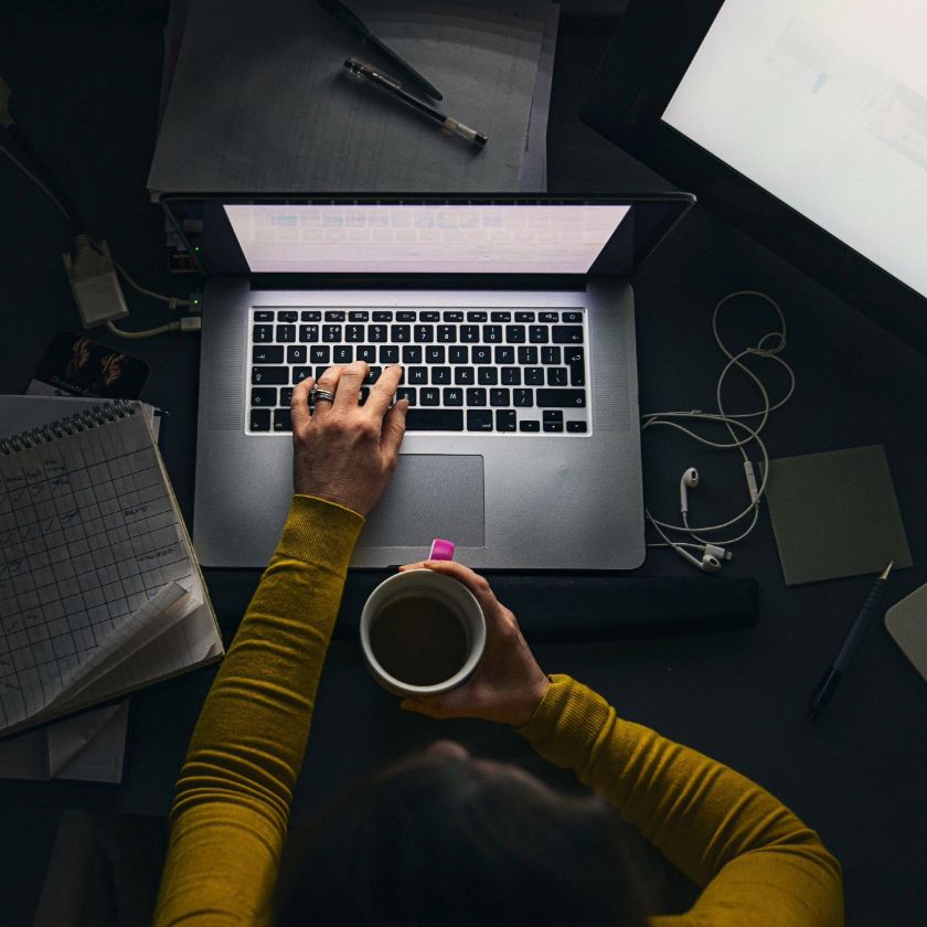 A person sits working at their laptop late at night with a cup of coffee.
