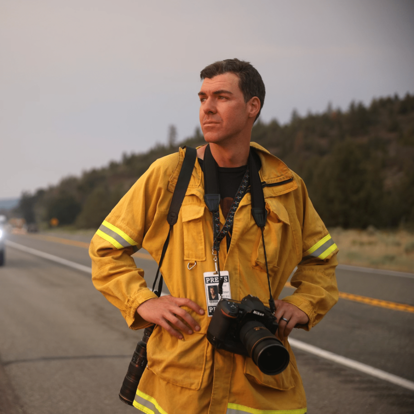 Photographer Josh Edelson surveys the landscape while standing in the road with a camera and press badge around his neck.