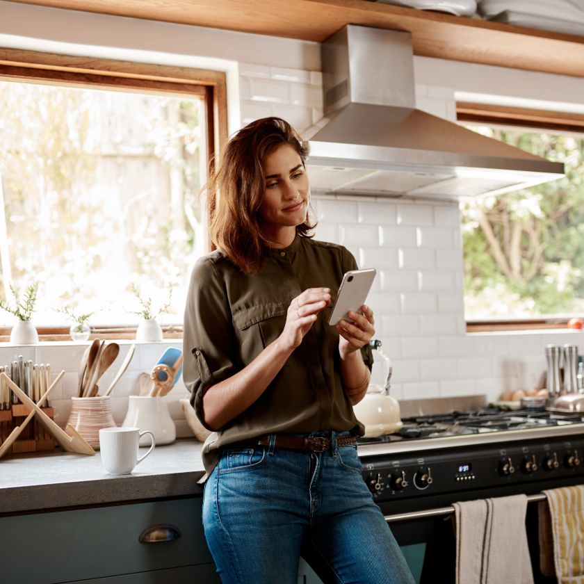A person smiles and casually checks their phone while standing in a kitchen.
