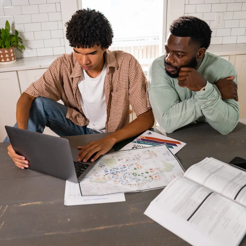 Two people sit together at a kitchen table with a new laptop, trying to figure out how to move their files to the new device.