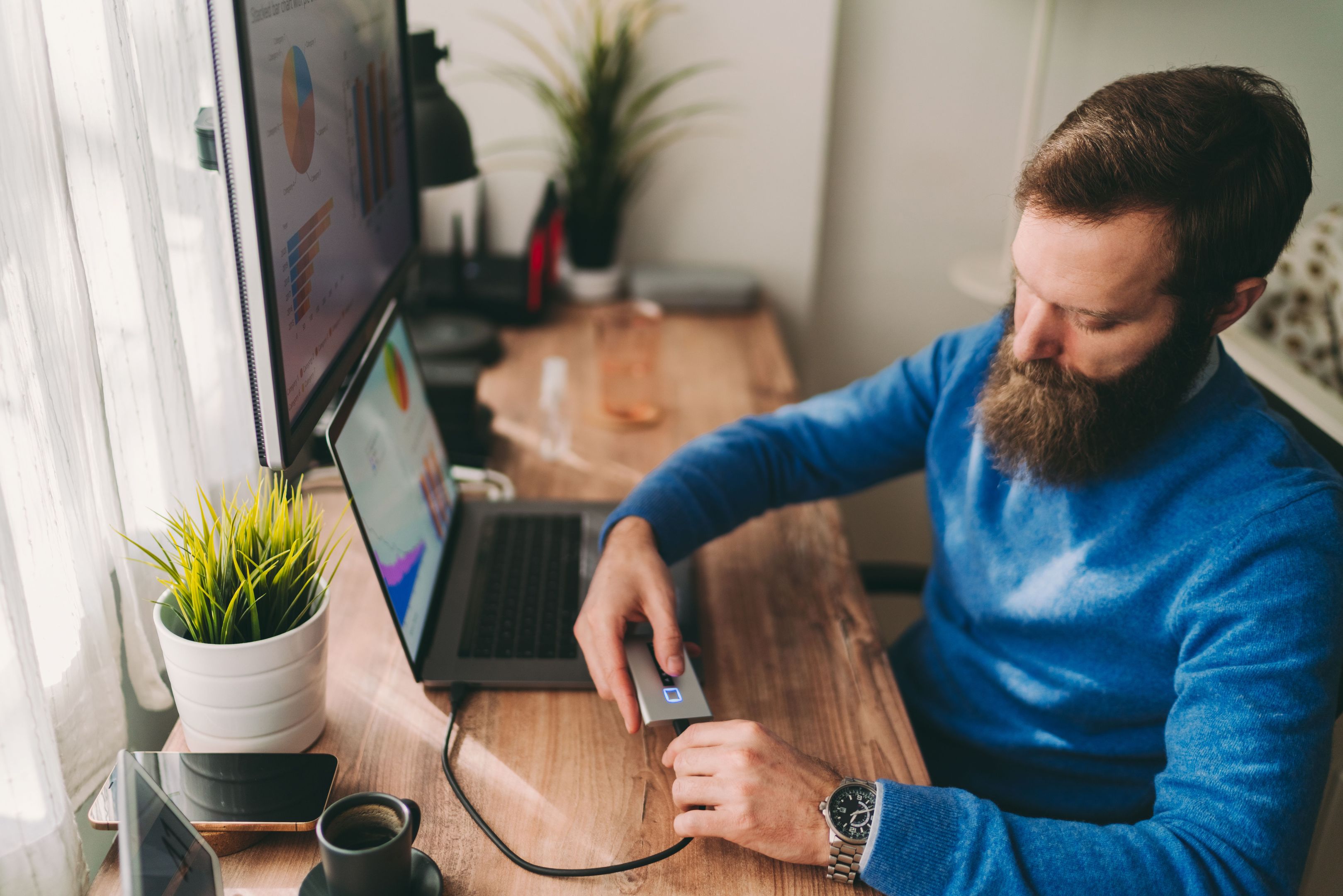 A person sat at a desk connects their external hard drive to their laptop using a USB cable.
