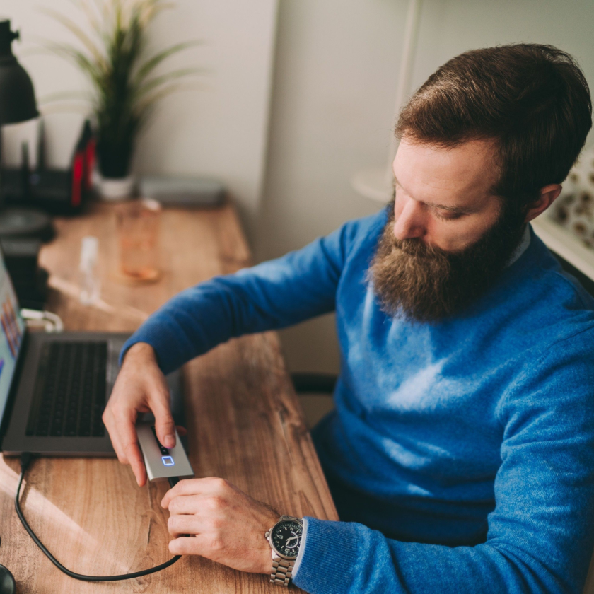 A person sat at a desk connects their external hard drive to their laptop using a USB cable.