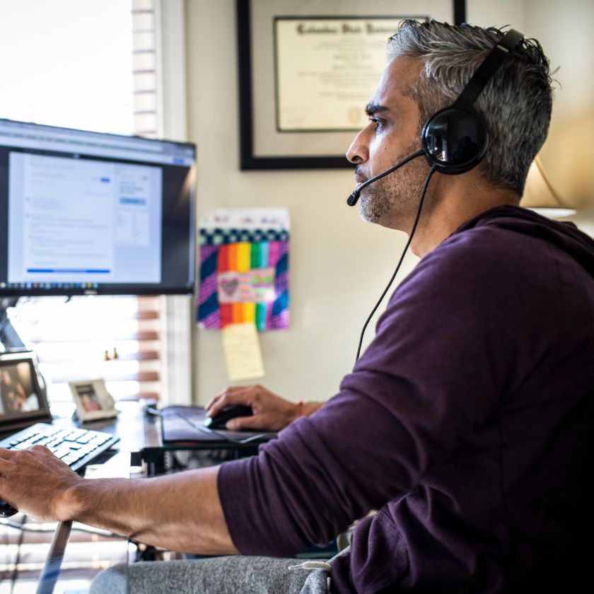 Person wearing a headset and working at a desk with multiple monitors, appearing focused on a task in a home office.