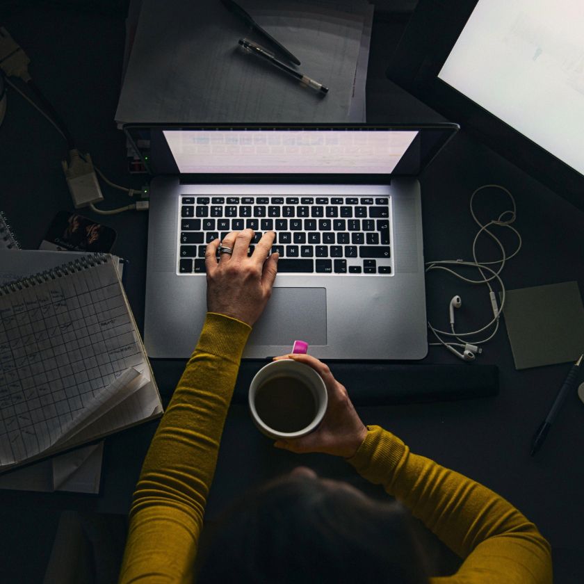 An entrepreneur working on their laptop late at night with a cup of coffee and spreadsheet by their side.