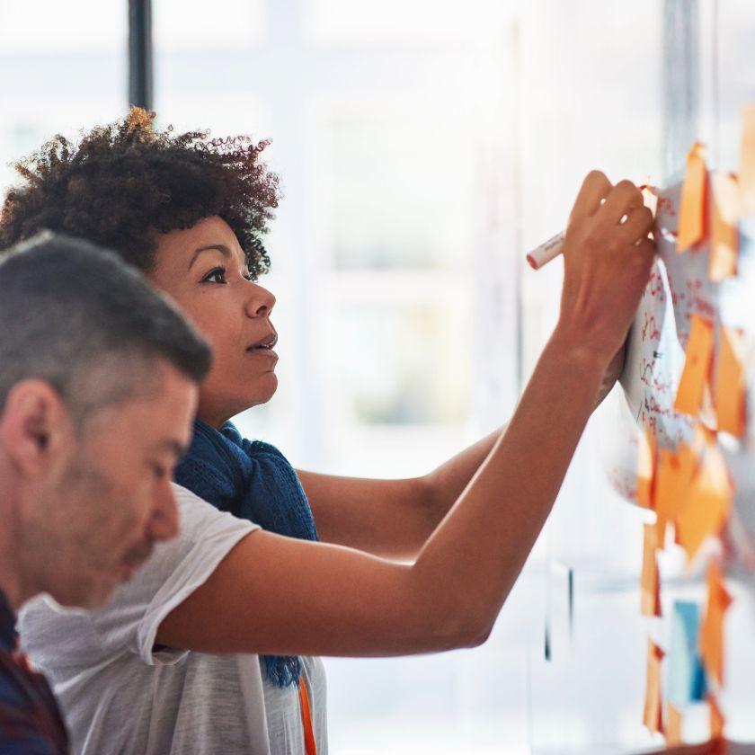Two people map out a marketing approval workflow on a whiteboard.