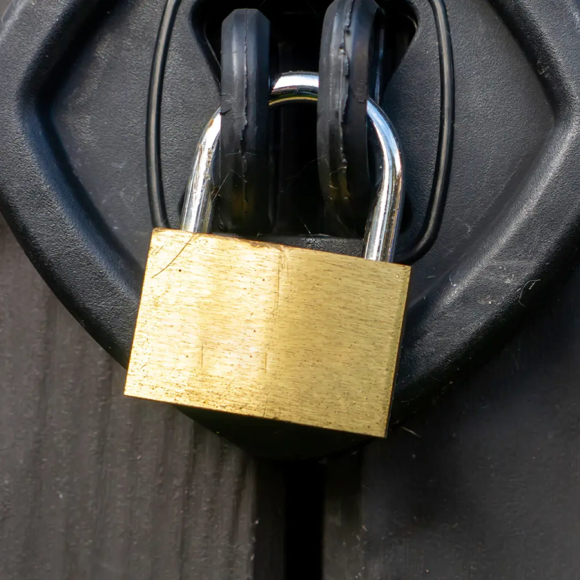 Gold padlock secured on a black latch on a wooden surface.