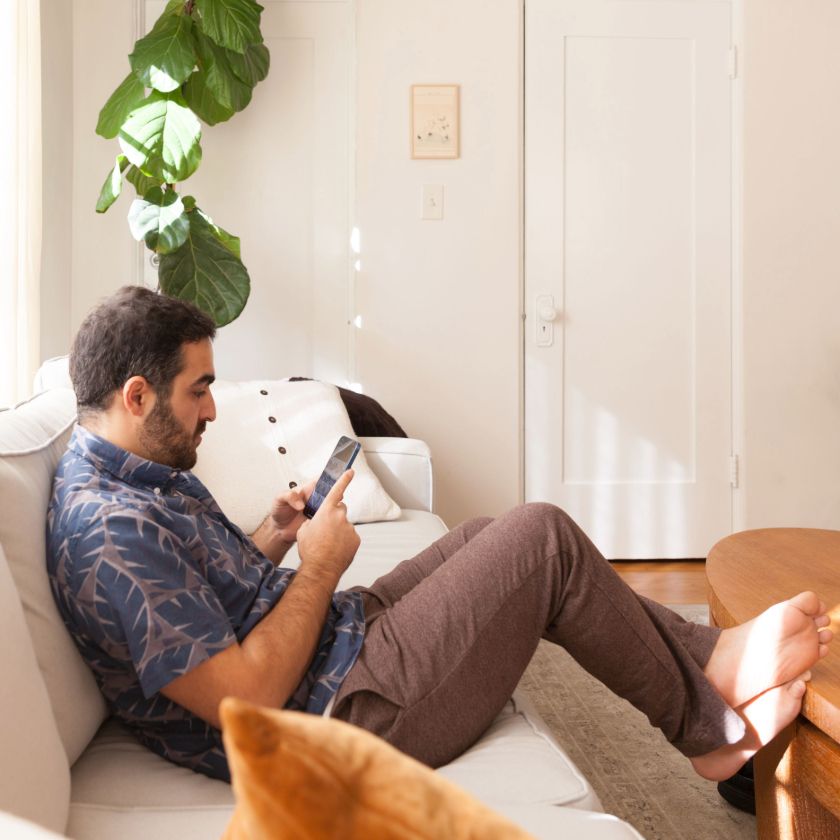 A person sits at home reading a book on their tablet device.