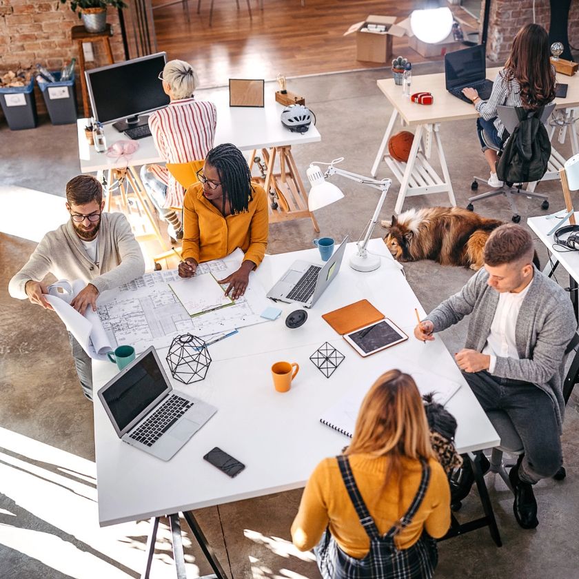 A team of colleagues collaborate on projects across multiple devices in an open-plan office space.