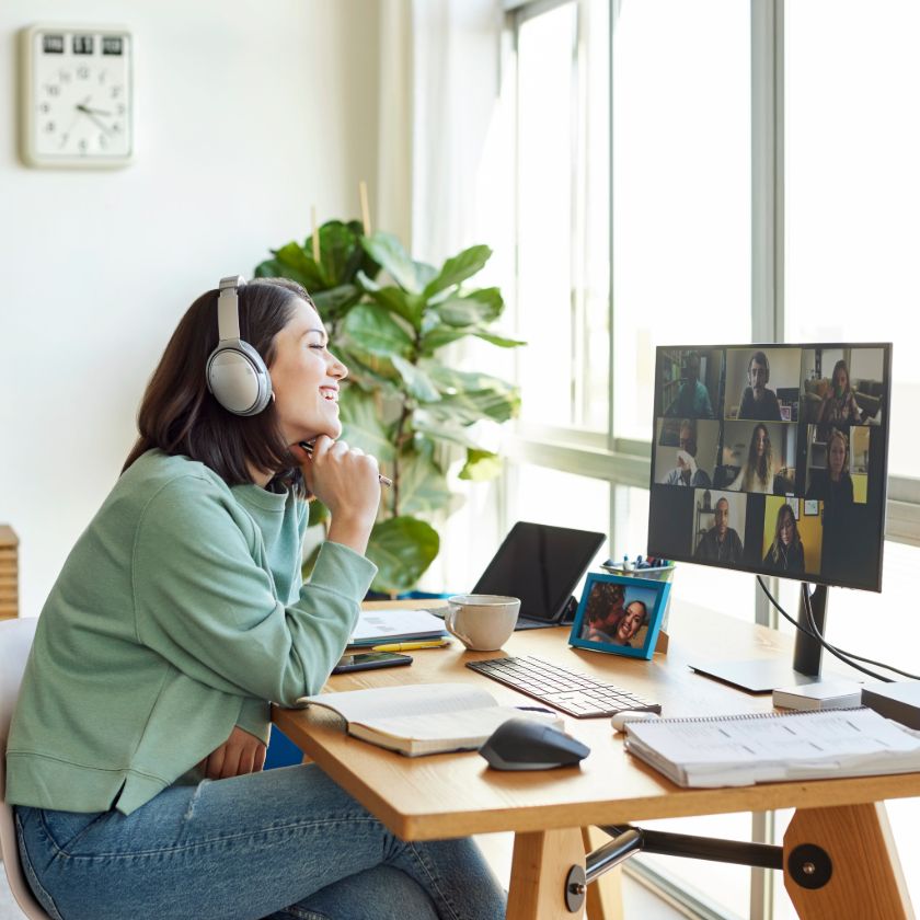 A person wearing headphones enjoys a virtual watch party, viewing a video project with a group on a computer screen at home.