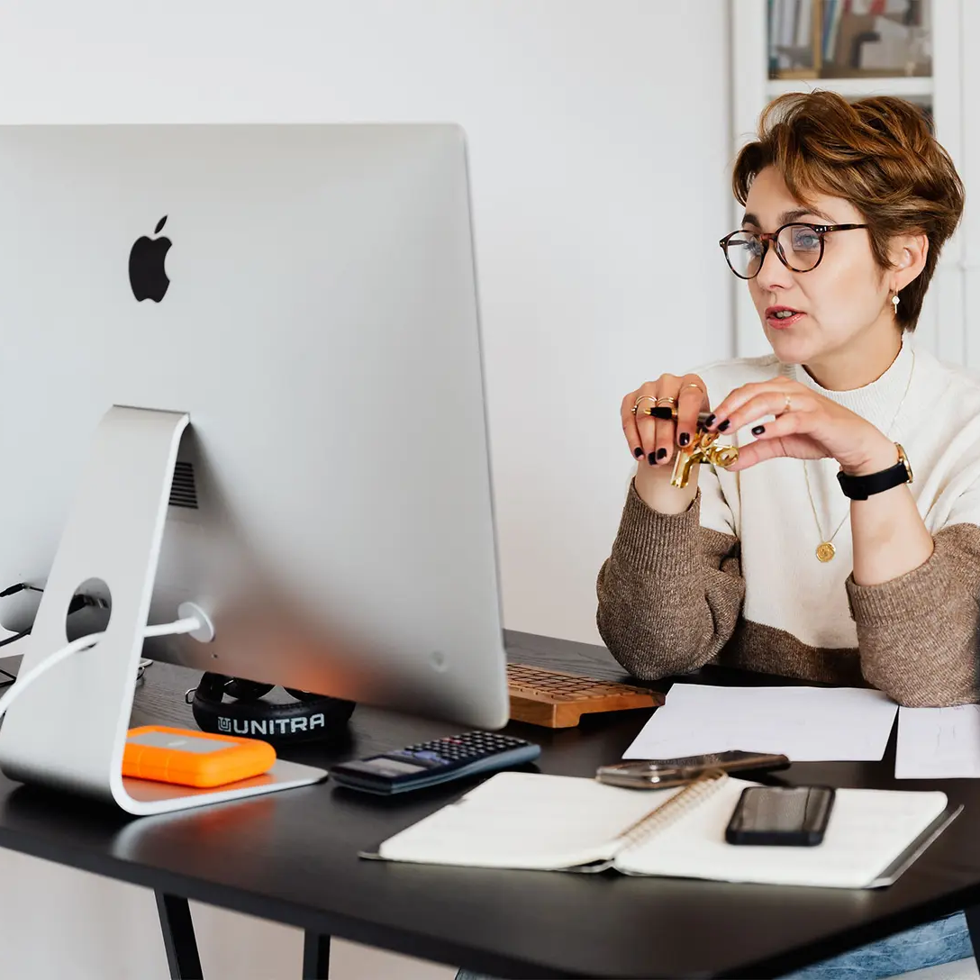 Professional person practicing video conferencing etiquette during a virtual meeting, seated at a tidy desk with a computer.