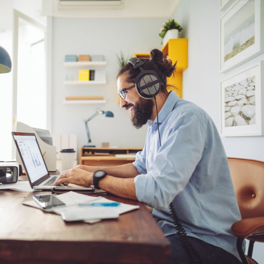 A person on a sales call wearing headphones smiles at their laptop while working remotely from their home office.