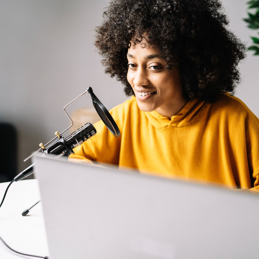 A person smiles as they look at their laptop screen while recording a video presentation from their home office.
